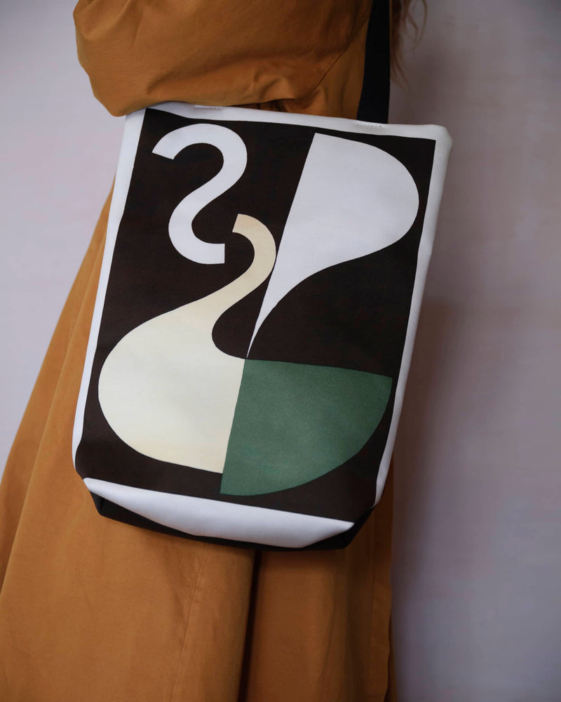 Abstract art tote bag displaying a Sophie Taeuber Arp artwork, worn by a female model in a burnt orange trench coat. The shot is close up and abstract just showing her torso.