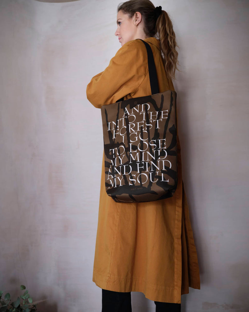 Artsy tote bag forest quote side worn by female model in a burnt orange autumn colour coat.