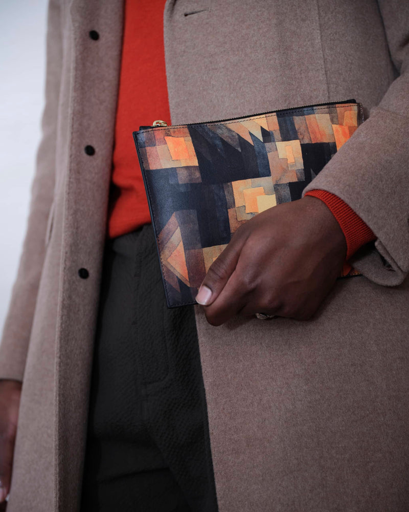 Leather art pouch printed with Paul Klee art carried by male model in a light brown coat.