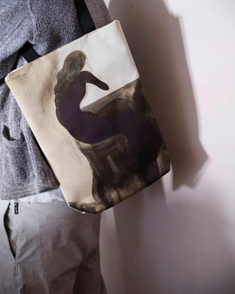Unique art tote bag displaying a Leon Spilliaert artwork worn by a male model casting a shadow on a smooth concrete wall..