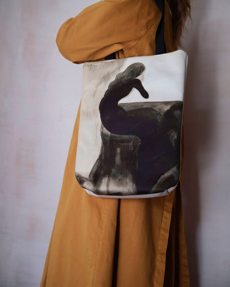 Close up of a unique art tote bag displaying a Leon Spilliaert artwork worn by a female model in a burnt orange trench coat.