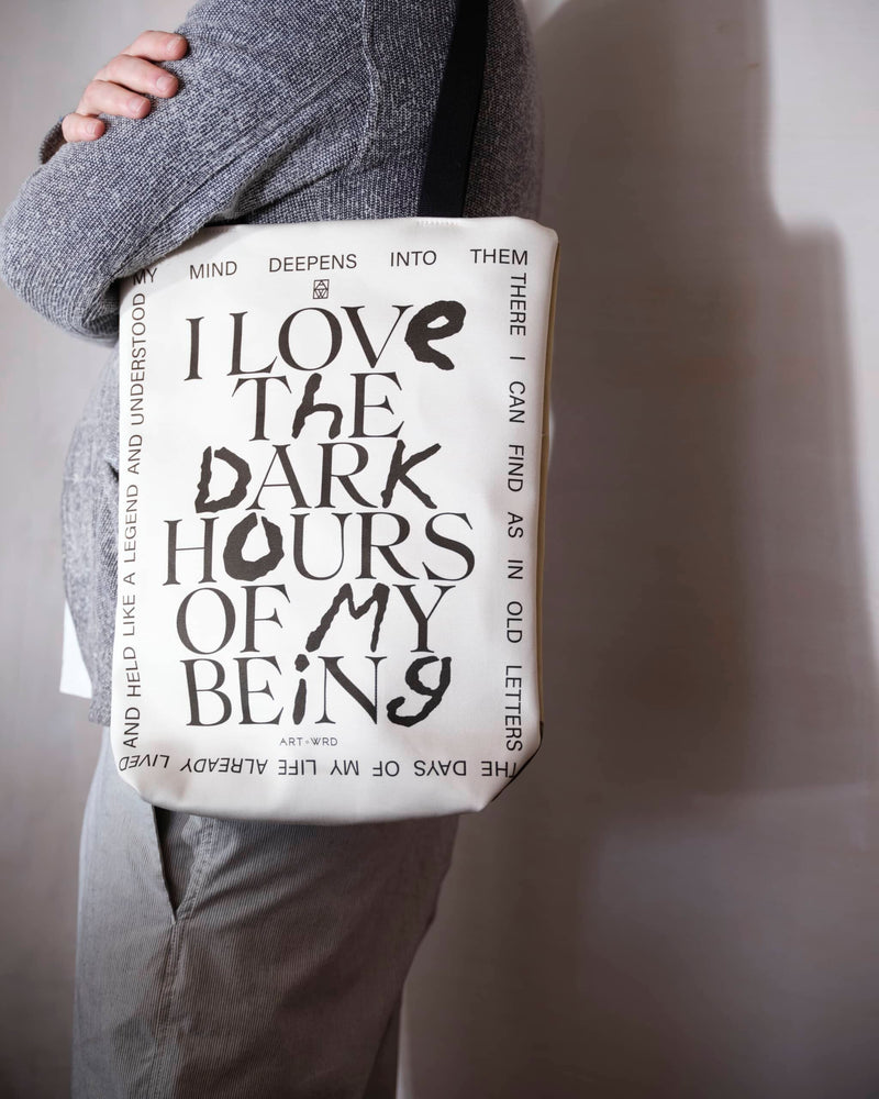 Reverse of a unique art tote bag displaying a Rainer Maria Rilke quote worn by a male model.