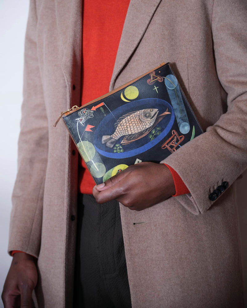 Unique bag with surrealist fish art by Paul Klee held by a male model in a light brown coat and orange-red pullover.
