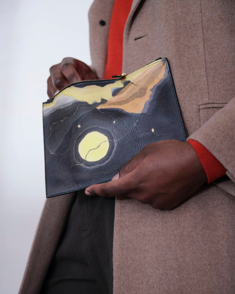 Unusual bag printed with Arthur Dove 'Me and The Moon' artwork held by male model in  light brown coat and orange-red jumper.