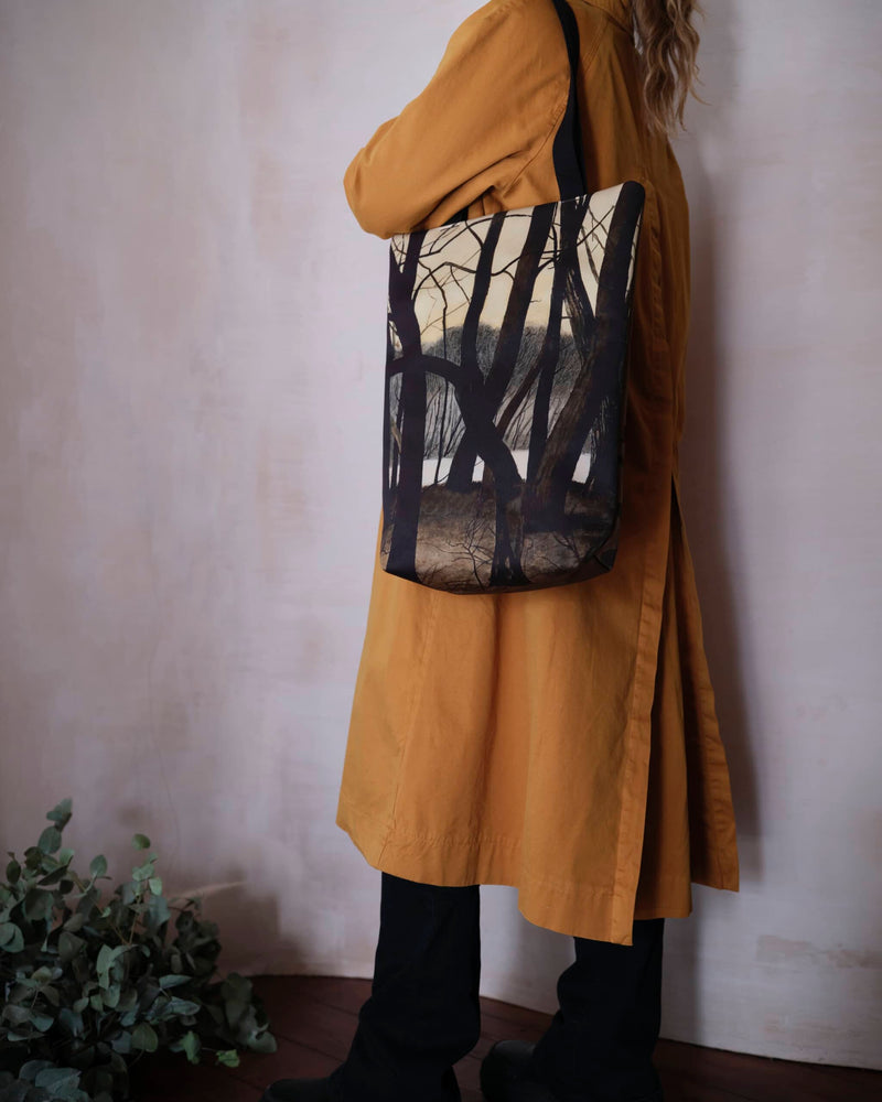 Artsy tote bag showing winter tree scene painting by Leon Spilliaert worn by female model in a burnt orange autumn colour coat.