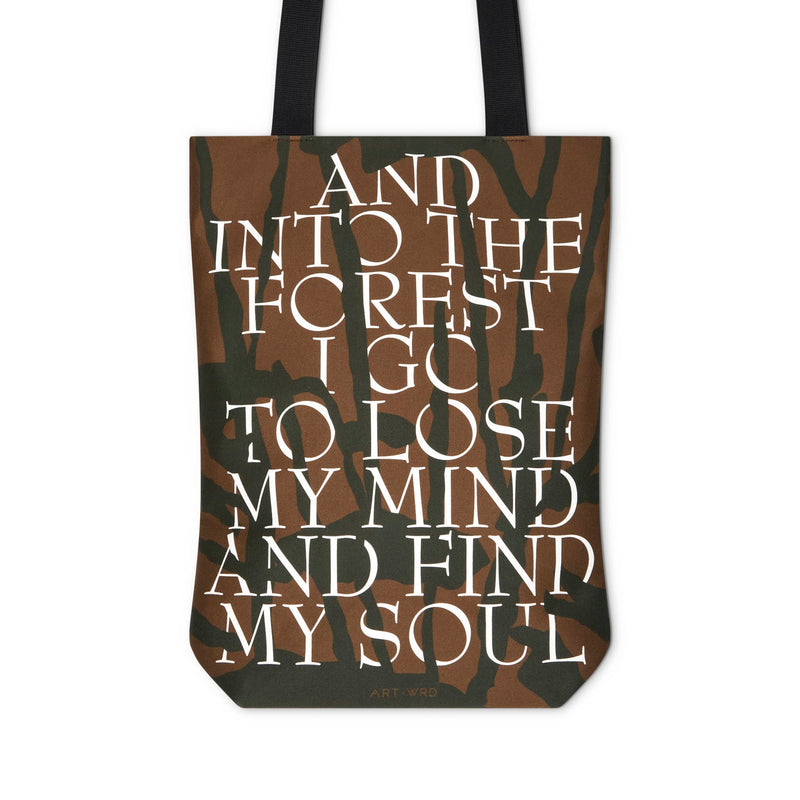 Artsy tote bag reverse showing a forest themed quote, presented among black tree branches on a brown background.
