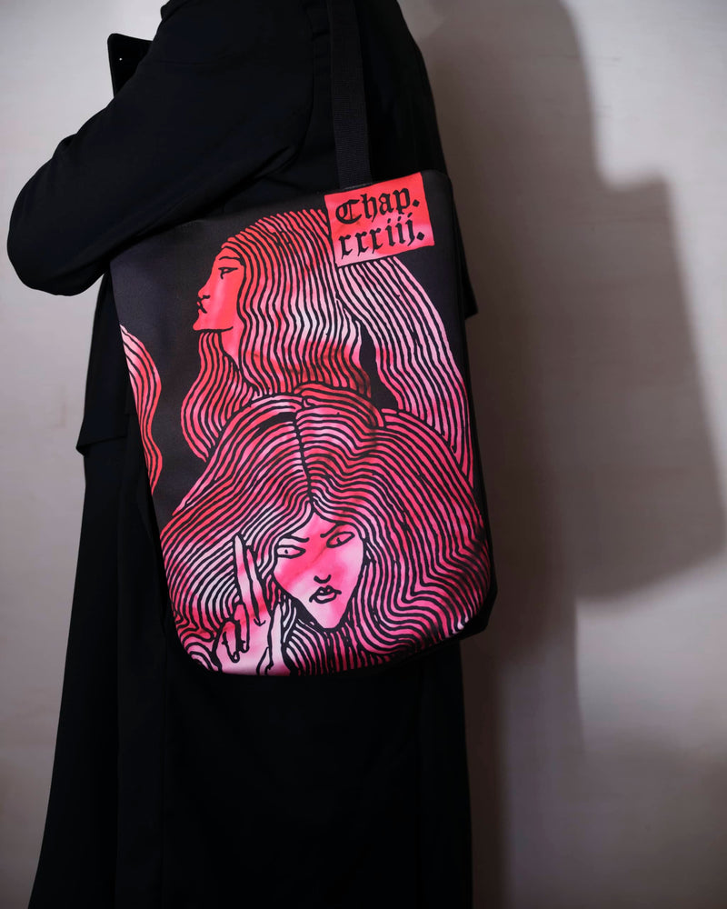 Bright pink tie-dye bag with Aubrey Beardsley witches design. It is worn by a male model in a long black coat, casting a shadow on to a grey wall.