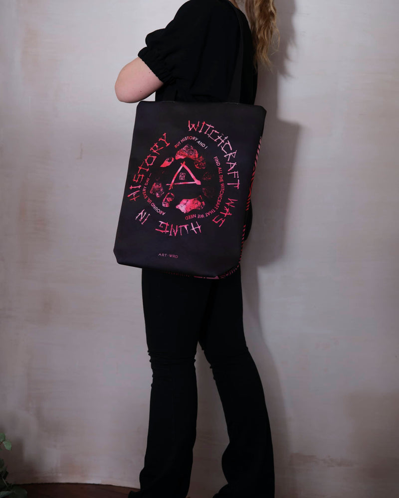 Bright pink tie-dye bag showing Emily Dickinson witches poem 'Witchcraft Was Hung', worn by a female model wearing black clothes.