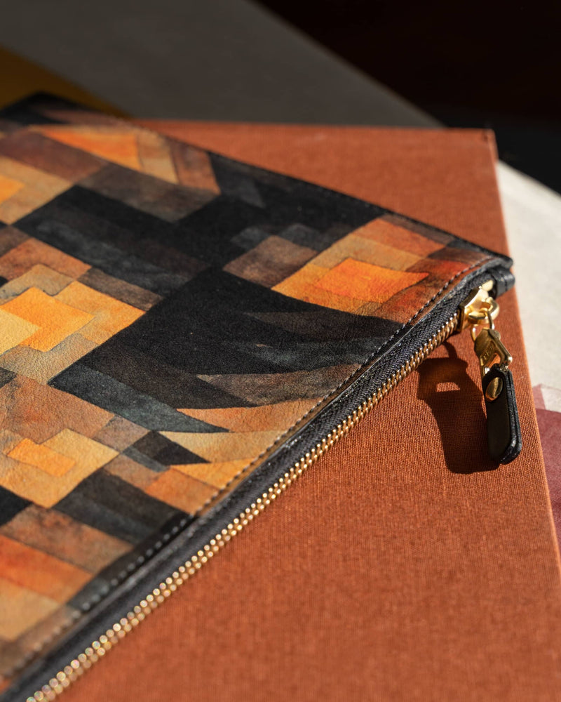 Leather art pouch printed with Paul Klee art laying on a brown fabric covered book.