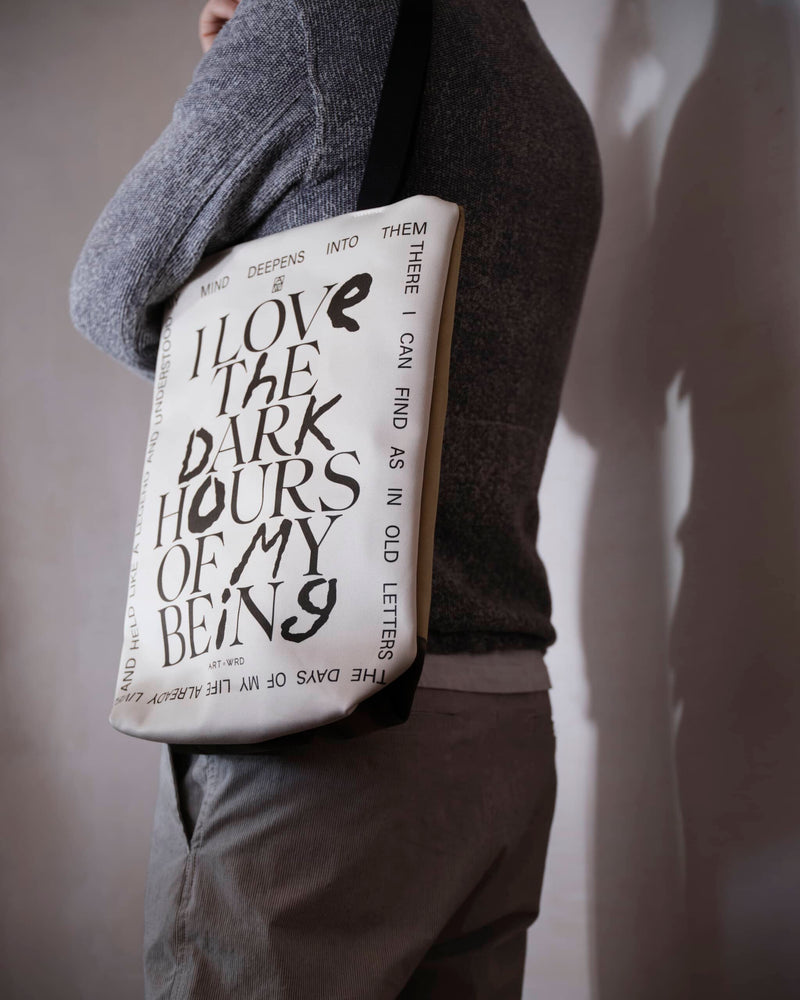Reverse of a unique art tote bag displaying a Rainer Maria Rilke quote worn by a male model shot from behind. 