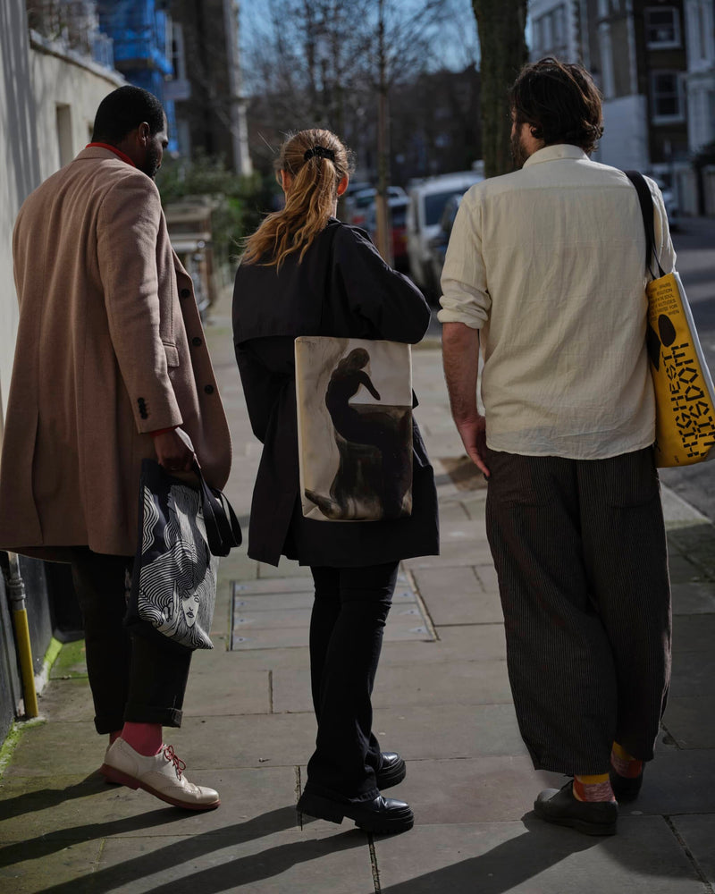 Three people wearing unique art totebags viewed shot from behind on a London street