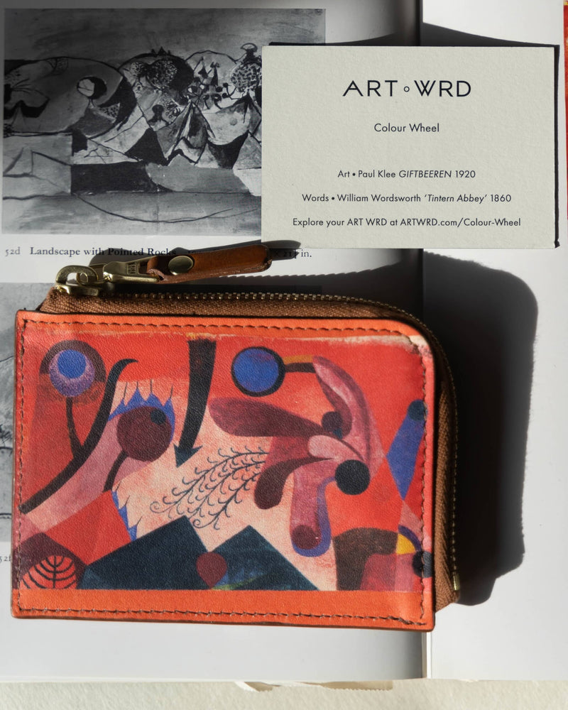 Close up of a unique purse with Paul Klee art print next to its artist and writer information card. There are placed on an art book.