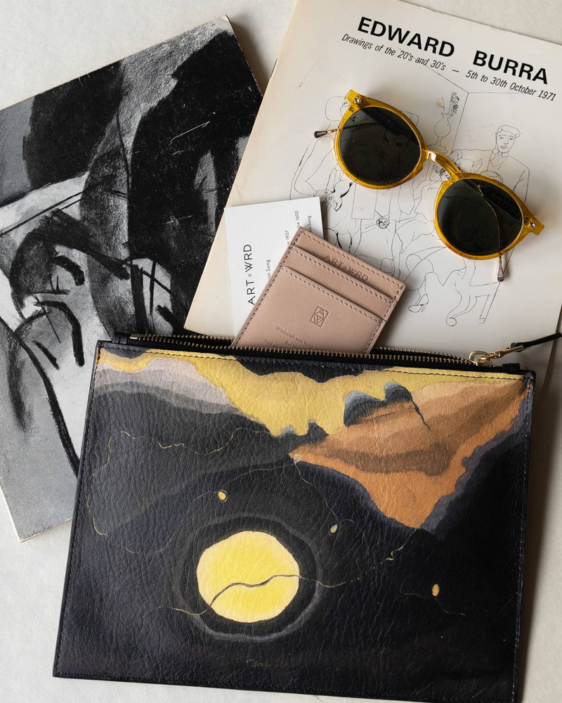 Unusual bag printed with Arthur Dove 'Me and The Moon' artwork next to arty mustard yellow sunglasses and art books.  An ART WRD card holder and information card is coming out of the unusual pouch bag.